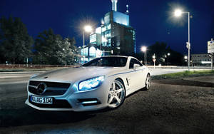 白色Mercedes跑車在夜間停泊，背後城市燈光閃爍。 — 夜晚 GIF 壁紙