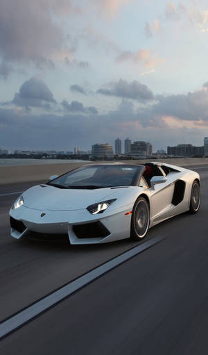 白色林寶堅尼 Aventador 開篷跑車在黃昏時分於海岸高速公路上飛馳。 — 林寶堅尼 4K 壁紙