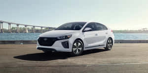 白色現代 Ioniq 混合動力車停在水邊，背景有橋樑。 — 低調 壁紙