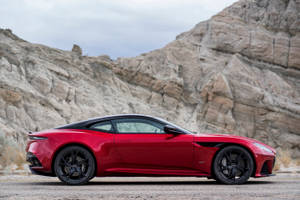 紅色Aston Martin跑車停泊在岩石懸崖附近的碎石路上。 — 汽車 壁紙