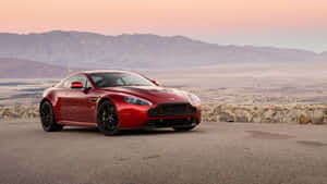 紅色Aston Martin跑車停泊在日落時分的山景觀景點上。