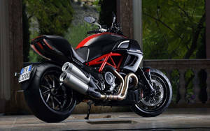 紅色和黑色Ducati電單車停放在石頭庭院上，背景有綠樹。 — 機車 壁紙