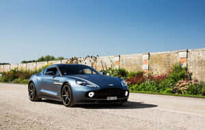 藍色Aston Martin跑車停泊在碎石上，靠近花園和磚牆。 — Steam Deck 壁紙