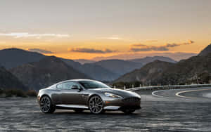 銀色 Aston Martin 跑車在夕陽下的山路上。 — Steam Deck 壁紙