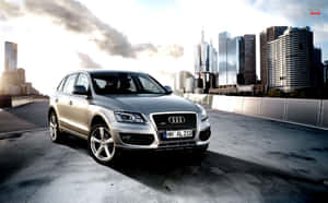 銀色 Audi Q7 SUV 在都市天橋上，背景有城市建築和多雲的天空。 — Steam Deck 壁紙