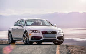銀色 Audi 房車停在沙漠公路上，背景是日落時分的山脈。 — Steam Deck 壁紙