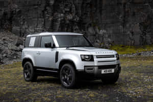 銀色 Land Rover Defender 停在懸崖附近的岩石地形上。 — Surface Laptop 壁紙