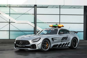銀色 Mercedes-AMG GT F1 安全車，閃爍著燈光，停在玻璃建築前。 — Surface Pro 壁紙