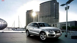 銀色Audi Q7 SUV停泊在海濱，附近有帆船和現代建築。 — 奧迪 GIF 壁紙