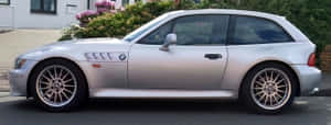 銀色BMW Z3停泊在街道上，附近有粉紅色開花灌木。 — 超寬螢幕 壁紙