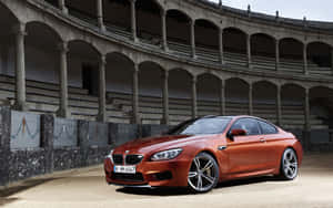 銅色BMW M6雙門跑車停泊在一個有石拱門的歷史鬥牛場內。 — Steam Deck OLED 壁紙