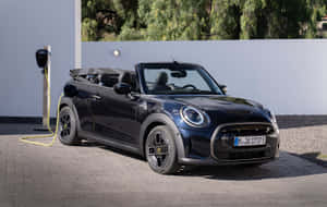 黑色電動MINI Cooper開篷車在瀝青車道上連接到充電器。 — 1280x800 壁紙