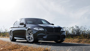 黑色BMW M5轎車停泊在乾草和陰天嘅鄉村道路上。 — 汽車 壁紙