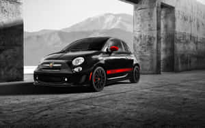 黑色Fiat 500 Abarth帶紅色條紋，停泊喺山附近嘅混凝土建築物內。 — MacBook Air M1 壁紙