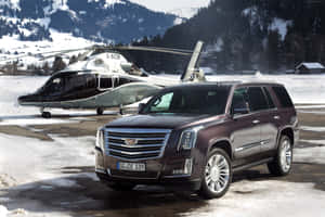 棗紅色 Cadillac SUV 停泊在積雪的山區機場直升機旁邊。 — Surface Pro 壁紙