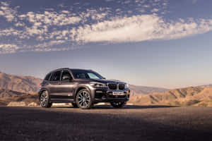 啞光灰色BMW X5 SUV停泊在沙漠公路上，有山脈和日落天空。 — Surface Pro 壁紙
