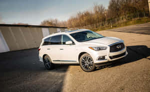 白色Infiniti QX60 SUV停泊在戶外，靠近倉庫和樹木。 — MacBook Air M1 壁紙