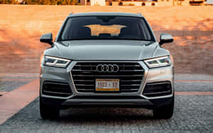 日落時分，一架銀色 Audi Q5 SUV 停喺鵝卵石車道上嘅正面視圖。 — Steam Deck OLED 壁紙