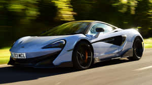 銀色McLaren跑車在陽光明媚的道路上與綠色樹木一起奔馳。 — 麥拿侖 GIF 壁紙