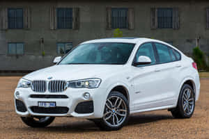 白色BMW X4 SUV停泊喺碎石路上，靠近一棟有木製百葉窗嘅建築物。 — Surface Pro 壁紙