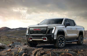 銀色GMC Sierra AT4 pickup truck在日落時停放在岩石沙漠地形上。 — Surface Laptop 壁紙