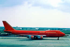 機場停機坪上的紅色 Braniff International 波音 747，背景有機庫。 — MacBook Pro M3 壁紙