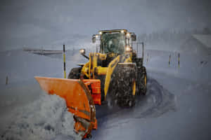 黃色剷雪車在雪景山區道路上清除積雪。 — MacBook Pro M2 壁紙