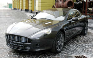 黑色Aston Martin跑車停泊在濕滑的鵝卵石街道上。 — Steam Deck OLED 壁紙