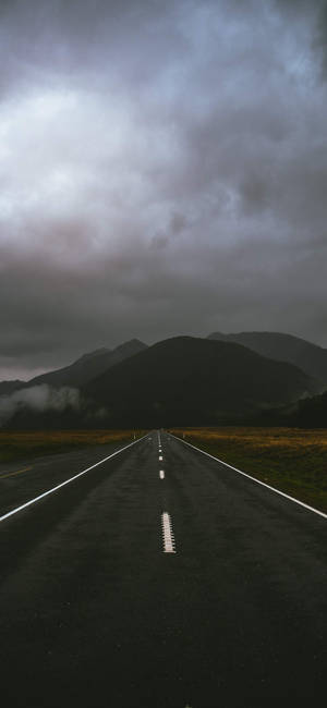 一條空蕩蕩的道路在陰暗多雲的天空下通往霧氣繚繞的山巒。 — OnePlus 壁紙