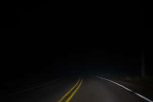 夜間一條黑暗蜿蜒的道路，有微弱的車道標線指引方向。 — 夜晚 GIF 壁紙