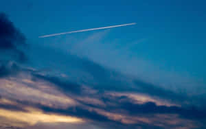 一架飛機在帶有紫色和金色雲彩的暮色天空中留下一道白色軌跡。 — 月色夜空 壁紙