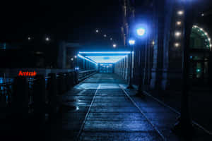 一條濕漉漉的步道，在藍色燈光下，夜間通往Amtrak車站。 — MacBook Pro M4 壁紙