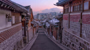 暮色中積雪的傳統韓國小巷，背景是現代城市天際線 — 城市景觀 壁紙