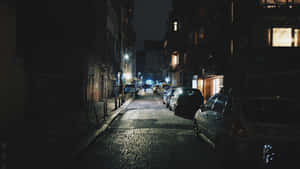夜晚昏暗的鵝卵石小巷，停有汽車和發光的窗戶。 — 夜空 壁紙