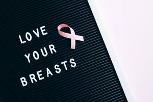 黑色字母板上的粉紅色絲帶和文字 love your breasts。 — 黑白 壁紙