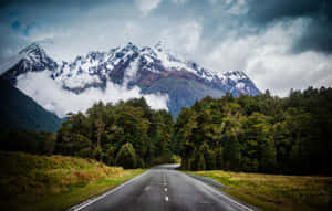 蜿蜒的道路穿過森林，在陰天中通往雪山 — MacBook Pro 16 壁紙