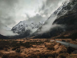 蜿蜒道路穿過霧氣瀰漫的山谷，背景是雪山 — 美麗的日落動畫 壁紙