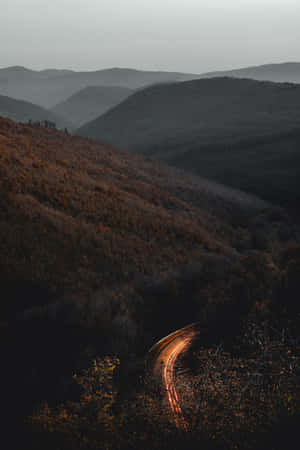 一條發光的道路在黃昏時分蜿蜒穿過霧氣瀰漫的秋日山丘。