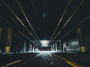 長長的黑暗隧道，有黃色管道和柱子，通往明亮的出口，有汽車和紅燈。 — Cavetown 壁紙
