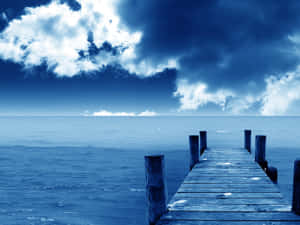 一條木碼頭在暴風雨的藍天下延伸至海洋。 — 天空美學 壁紙