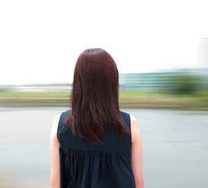 一位穿著黑色連衣裙的女性背對鏡頭站在路邊。