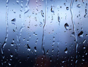 雨滴在模糊的藍色背景的窗戶上滑落。