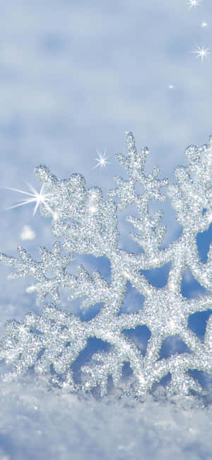 藍色天空中帶有星星閃爍的雪地上的閃閃發光雪花。 — iPhone 16e 壁紙