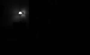一個光線昏暗的房間，一盞壁燈在黑暗中投下陰影。 — 暗夜城市 壁紙