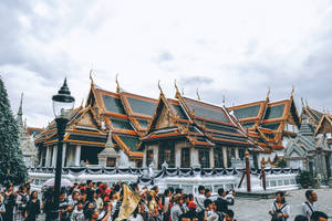 遊客聚集在金頂泰國寺廟附近，天空多雲。