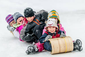 孩子們戴著冬季帽子和外套在雪丘上滑雪橇。