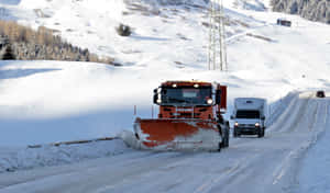 橙色掃雪車清理山路積雪，後面有一輛白色貨車。 — 低調 壁紙