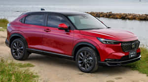 紅色本田 HR-V 混合動力 SUV 停泊在水邊，有岩石防波堤。 — 本田 壁紙