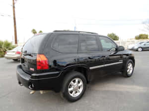 黑色GMC Envoy SUV停放在停車場，有棕櫚樹和其他車輛。 — 4:3 壁紙
