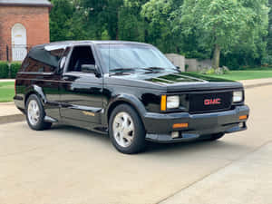 黑色GMC Typhoon SUV停放在磚房附近的混凝土車道上。 — 4:3 壁紙